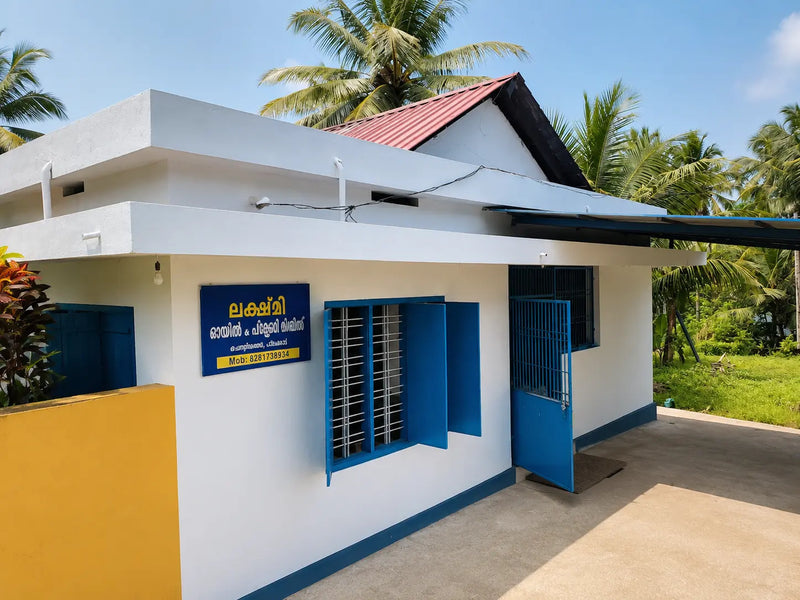 A small white building with blue trim and a red roof, photographed outdoors with palm trees and greenery in the background. A blue sign with yellow text is mounted on the wall next to a window.